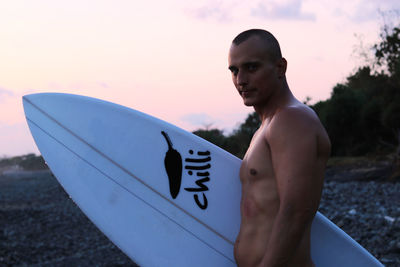 Portrait of shirtless man standing against sky during sunset