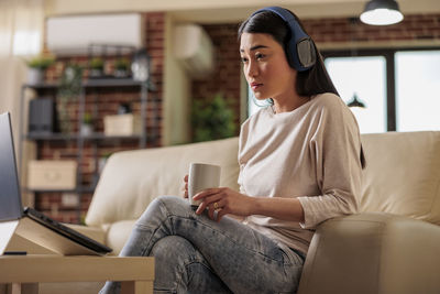 Woman wearing wireless headphones using laptop at home