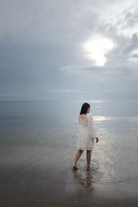 Rear view of woman standing at beach against sky