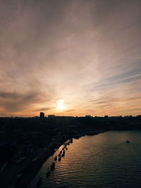 Scenic view of river by buildings against sky during sunset