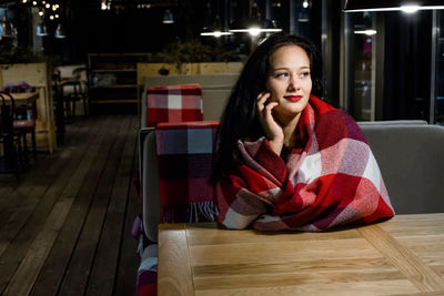 Young woman wrapped in blanket sitting at restaurant