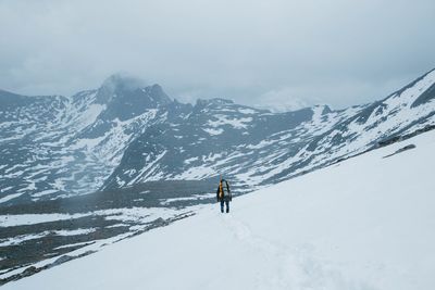 Person climbing on snowcapped mountain against sky