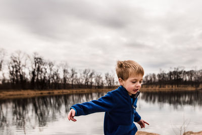 Young boy being silly at the edge of a lake on a cloudy day