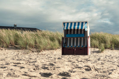 Hooded chairs on beach against sky