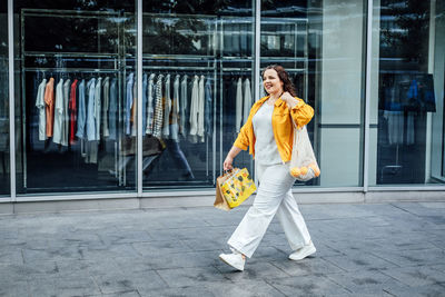 Happy confident smiling plus size curvy young woman with shopping bags walking on city street near