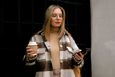 Young woman using mobile phone while standing in mirror