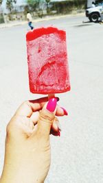 Cropped hand holding popsicle against street