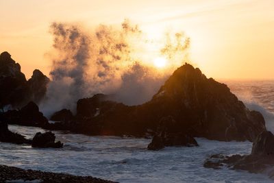 Rock formation in sea against sky during sunset