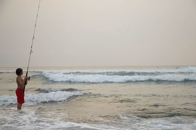 Rear view of man standing on beach against sky