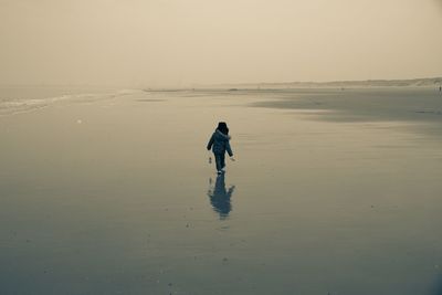 Rear view of boy walking at beach during sunset