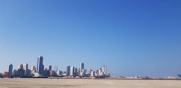 Sea by modern buildings against clear blue sky