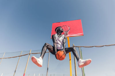 Low angle view of man jumping hanging against clear sky