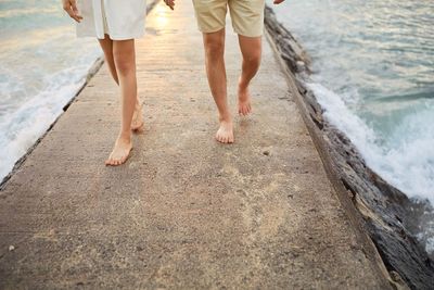Low section of man and woman walking on jetty at beach