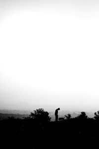 Silhouette man standing by tree against clear sky