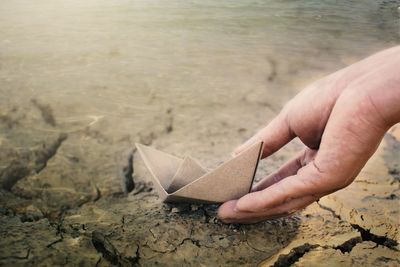 Close-up of hand with paper boat at beach