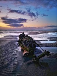 Shipwreck on beach against sky during sunset