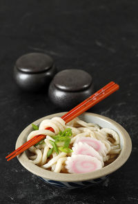 Japanese kake udon with narutomaki and green onion. served on ceramic bowl on black marble table