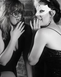 Female friends wearing masks by brick wall