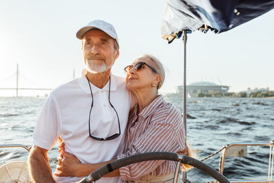 Low angel view of couple standing on sailboat against sea