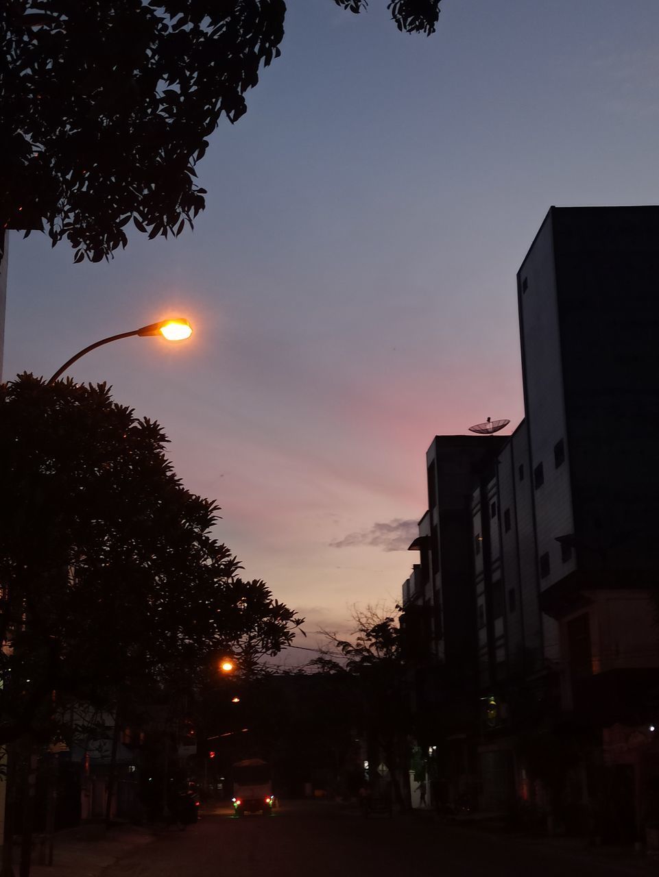 STREET AMIDST BUILDINGS AGAINST SKY DURING SUNSET