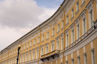 The yellow wall of an old multi-storey building with a cloudy sky in the background