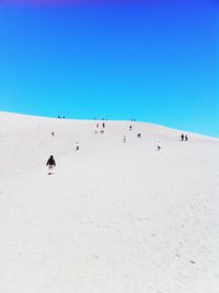 People on sand against clear blue sky