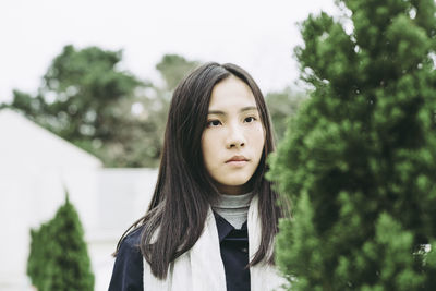 Portrait of young woman standing by trees