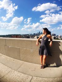 Young woman leaning on retaining wall against sky