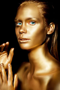 Close-up portrait of woman with golden glitter make-up against black background