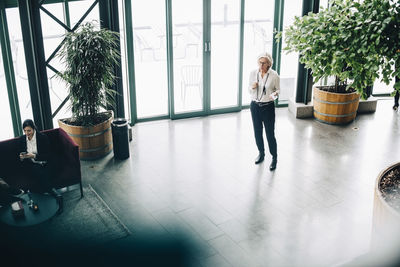 High angle view of businesswoman talking on mobile phone while coworker sitting on chair at office