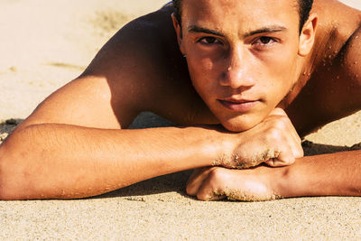 Portrait of shirtless boy lying on sand at beach