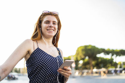 Positive woman with smartphone listening to music on street