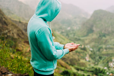 Man holding cap while standing on mountain