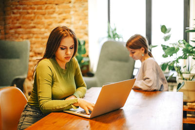 Young woman using laptop while sitting with friend