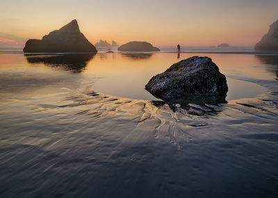 Rocks on sea shore against sky during sunset