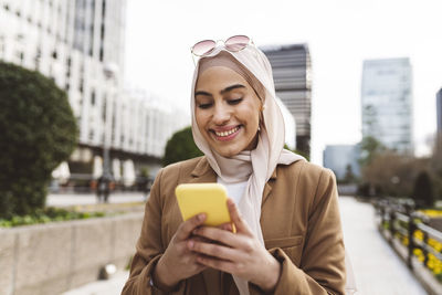 Happy young woman text messaging through smart phone at office park