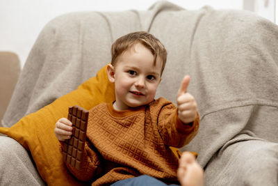 Little adorable boy sitting on the couch at home and eating chocolate bar. child and sweets