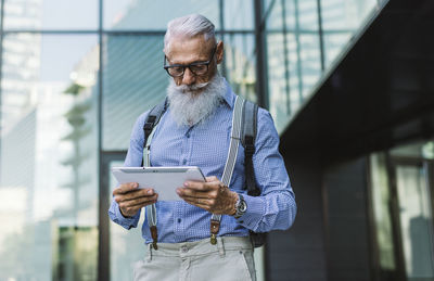 Senior hipster holding digital tablet against building