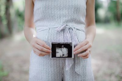 Midsection of pregnant woman holding x ray while standing outdoors