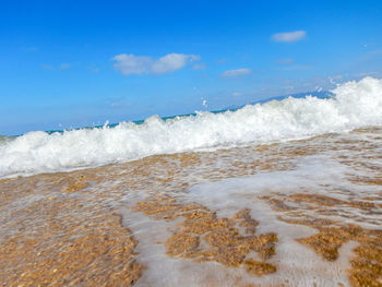 Waves rushing towards shore against sky