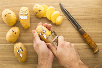 Close-up of man peeling potatoes with smiley faces on table