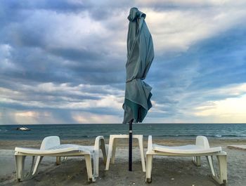 Deck chairs on beach against sky