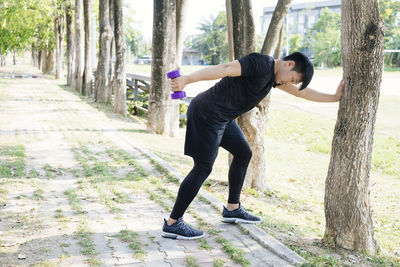 Side view of young man with arms raised against trees