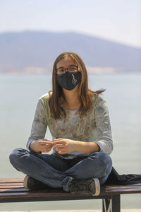 Portrait of young woman wearing sunglasses while sitting at beach