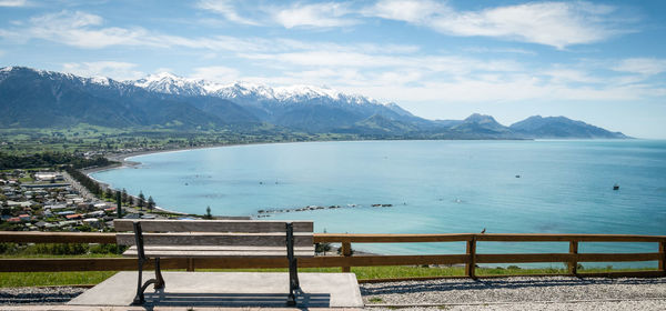 Castal town with azure waters, mountains in backdrop and bench in foreground, kaikoura, new zealand