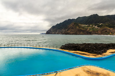 Swimming pool by sea against sky