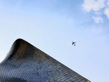Low angle view of airplane flying over museo soumaya against sky