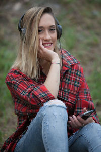 Portrait of smiling young woman listening music while sitting on land