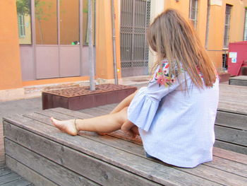 Rear view of girl sitting on wood