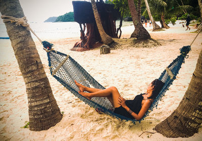 Low section of woman relaxing on hammock at beach